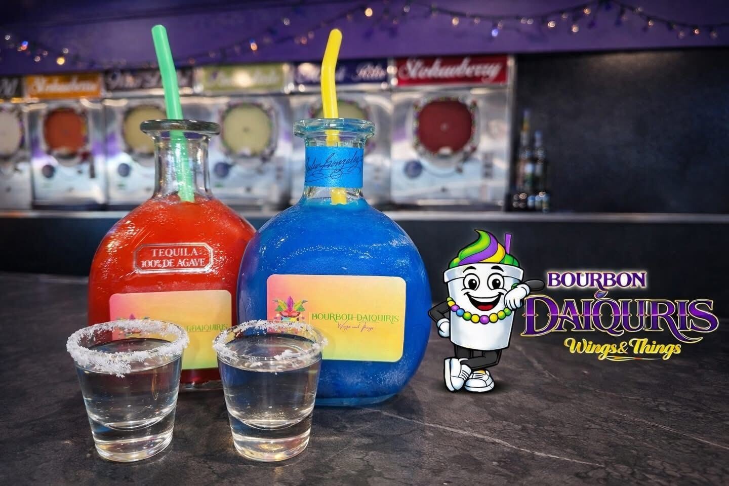 Two frozen daiquiris served in tequila bottles with salt-rimmed shot glasses, in front of the daiquiri machines