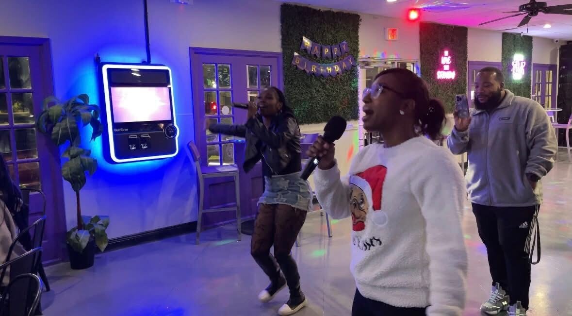 Two people singing karaoke in the shop while a friend films