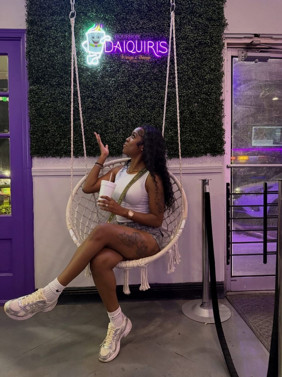 A guest on a hanging chair under the Bourbon Daiquiris neon sign
