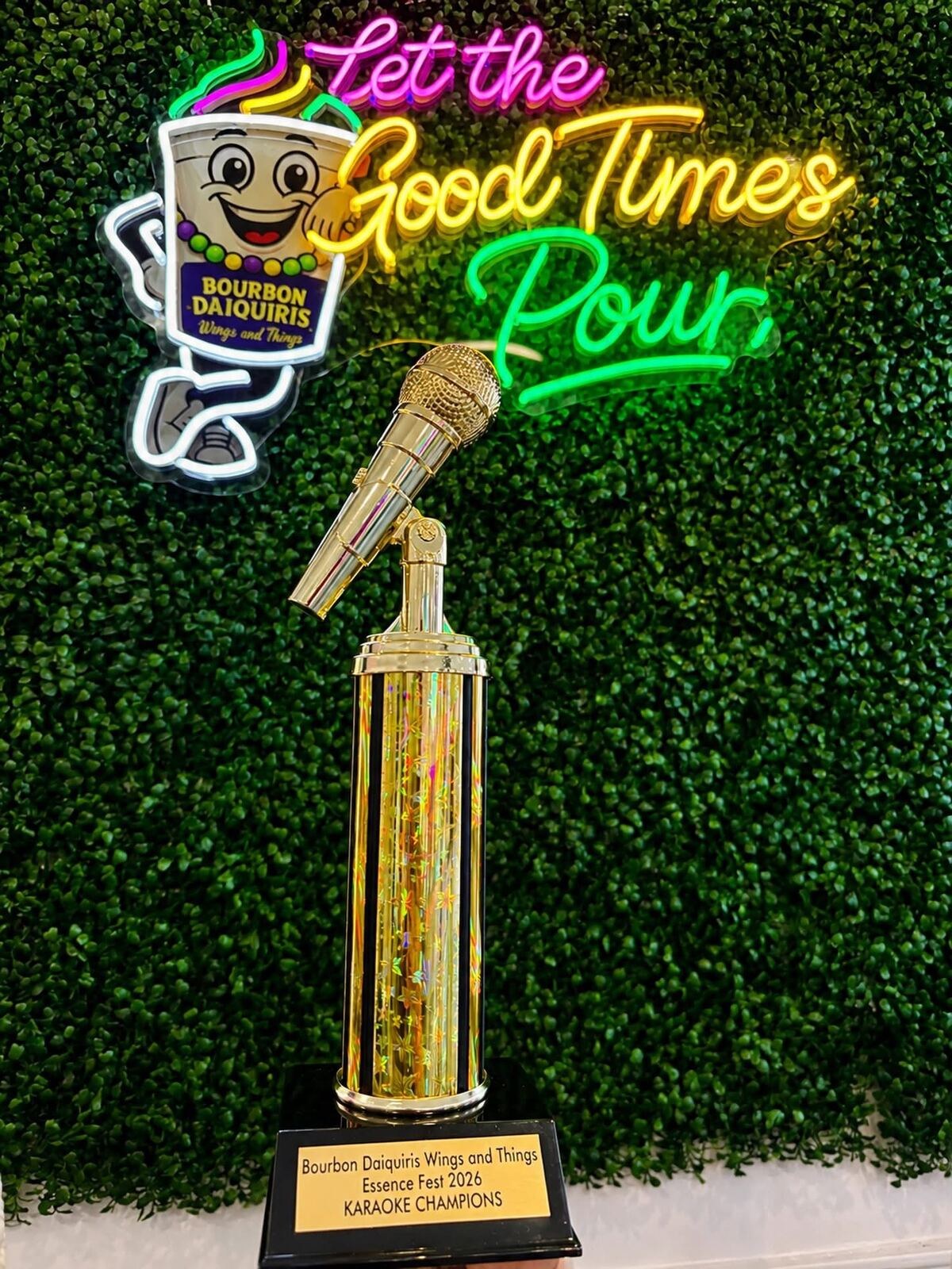 A gold microphone trophy reading Essence Fest 2026 Karaoke Champions, in front of a neon sign